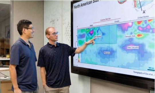 Jonny Wu y Spencer Fuston, científicos, señalando una pantalla donde hay un mapa de las placas tectónicas de la Tierra